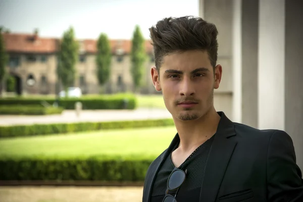 Beau jeune homme à l'extérieur, élégants jardins derrière lui — Photo