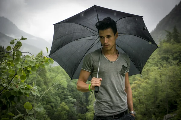 Junger Mann in üppigen, grünen Berge halten einen Regenschirm — Stockfoto