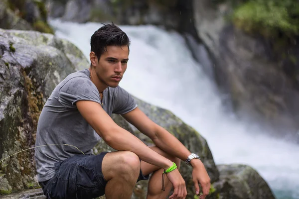 Handsome young man near mountain waterfall on rocks — Stock Photo, Image