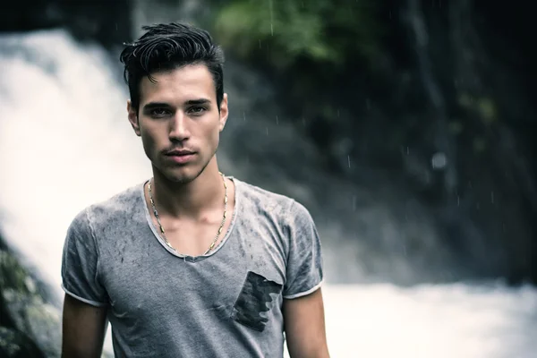 Joven guapo junto a la cascada de montaña — Foto de Stock