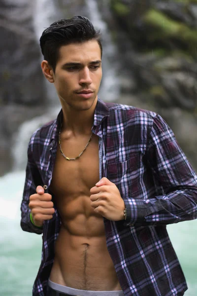 Handsome young man near mountain waterfall with open shirt — Stock Photo, Image