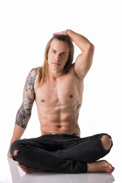Długowłosy mężczyzna z tatuażami siedzi — Zdjęcie stockowe