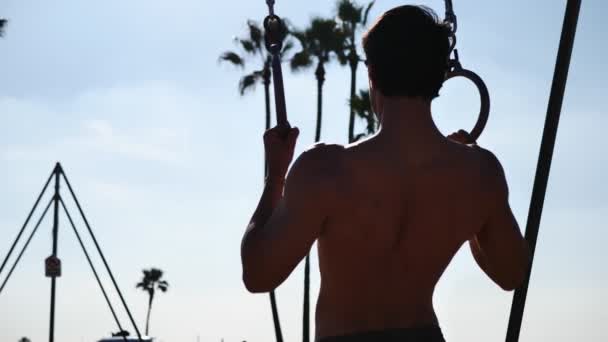 Bello giovane uomo che si esercita con anelli in spiaggia — Video Stock