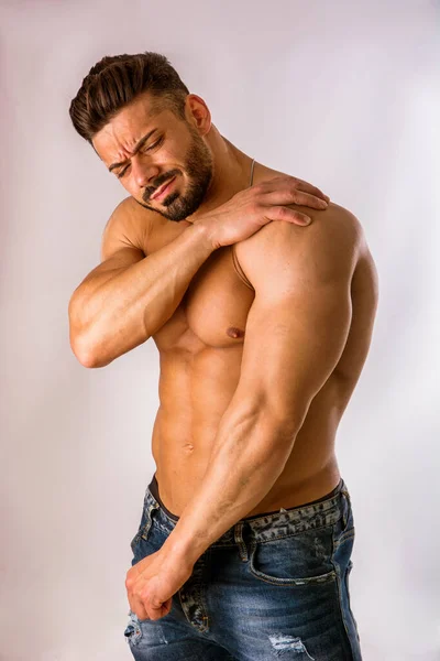 М'язистий чоловік тримає плече однією рукою і похмуро болить — стокове фото