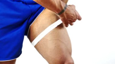 Kaslı vücut geliştirici, bacağının ölçüsünü şeritle alıyor.