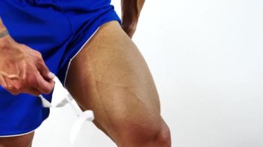 Kaslı vücut geliştirici, bacağının ölçüsünü beyaz arka planda alıyor. Tanınmayan kişi