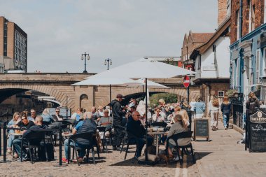 York, İngiltere - 22 Haziran 2021: Eski Romalılar tarafından İngiltere 'nin kuzeydoğusunda duvarlarla çevrili bir şehir olan Ouse Nehri' nin kıyısındaki bir barın açık hava masalarındaki insanlar.