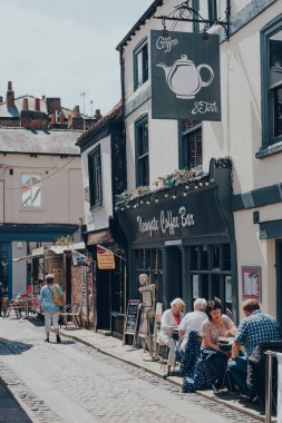 York, İngiltere - 22 Haziran 2021: Antik Romalılar tarafından İngiltere 'nin kuzeydoğusunda duvarlarla çevrili bir şehir olan York' ta dar bir caddedeki Newgate Coffee Bar 'ın açık hava masalarındaki insanlar.