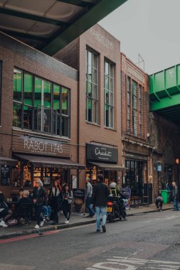 Londra, İngiltere - 17 Ekim 2021: Londra 'nın en büyük ve en eski gıda pazarlarından biri olan Borough Market' teki bir dizi dükkan ve kafe dışındaki insanlar.