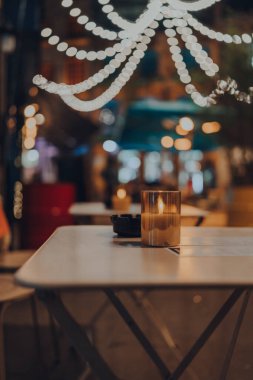 Kışın bir restoranın açık hava masasında mum yakmak, arka planda Noel ışıkları, seçici odak, bokeh.