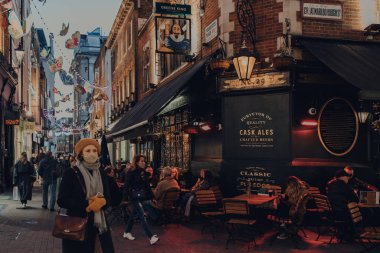 London, UK - June 13, 2020: People at the outdoor tables of Shakespeares Head pub in Soho, an area of Central London famous for its pubs and restaurants. People walking past, selective focus.
