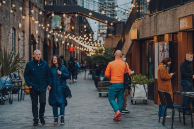 Londra, İngiltere - 01 Ocak 2022: Coal Drops Yard 'da ışıkların altında yürüyen insanlar, King' s Cross St Pancras istasyonları yakınlarındaki bir alışveriş merkezi ve yemek merkezi 2018 yılında açıldı..