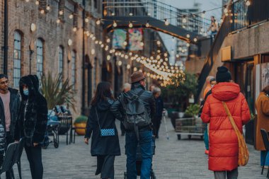 Londra, İngiltere - 01 Ocak 2022: Coal Drops Yard 'da ışıkların altında yürüyen insanlar, King' s Cross St Pancras istasyonları yakınlarındaki bir alışveriş merkezi ve yemek merkezi 2018 yılında açıldı..