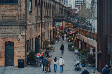 Londra, İngiltere - 01 Ocak 2022: Coal Drops Yard 'da ışıkların altında yürüyen insanlar, King' s Cross St Pancras istasyonları yakınlarındaki bir alışveriş merkezi ve yemek merkezi 2018 yılında açıldı..