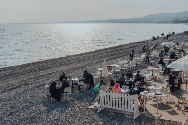 Nice, Fransa - 10 Mart 2022: İnsanlar Nice 'teki bir plaj masasında oturup dinleniyorlar, Fransız Rivierası' ndaki ünlü bir turizm merkezi..