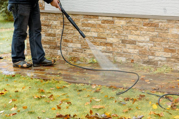 Man cleaning street with high pressure power washer, washing stone garden paths