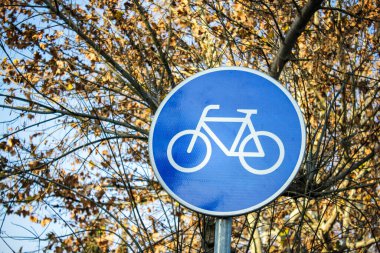 Arka planda ağaç dalları olan bisiklet yolu tabelası