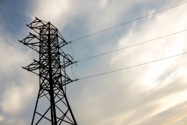 Gün batımında gökyüzüne karşı elektrik iletim pilonu görüntüsü.