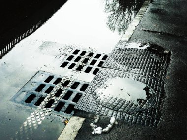 Su kanalizasyona akıyor. Kanalizasyon kapaklı ıslak bir yol..