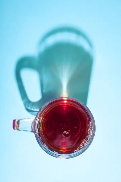 Yaratıcı gölgeli parlak güneş ışığı altında mavi arka planda bir bardak çay..