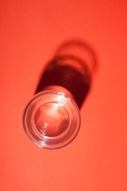 Kırmızı zemin üzerinde soyut koyu gölgesi olan bir bardak su..