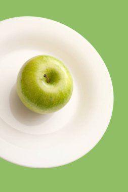 Yeşil arkaplanda izole edilmiş beyaz tabakta yeşil elma.
