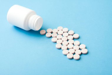 White plastic bottle and pills on blue background.