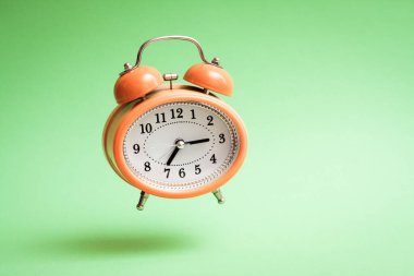 Turuncu renkli uçan çalar saat. Yeşil arkaplanda uçan alarm saati.