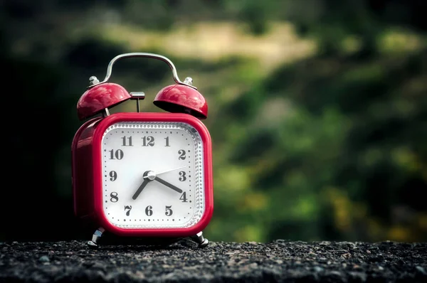 Red Retro Style Alarm Clock Concrete Surface Blurry Trees Background — Stock Photo, Image