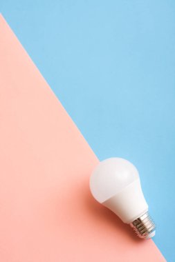 Mavi ve pembe arka planda beyaz ekonomi ampulü.