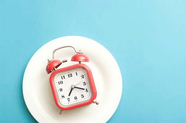 Minimalist flat lay concept red alarm clock on a white plate.