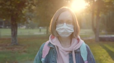 Koruyucu tıbbi maskeli güzel bir kadının portresi, parkın ortasında sırt çantalı bir gözlük..