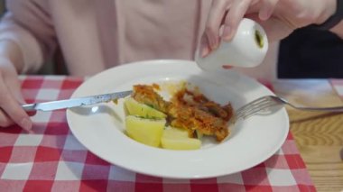 Bir kadın tuzlar ya da mevsimlik yiyecekler - haşlanmış patates ve domates sosunda haşlanmış balık.