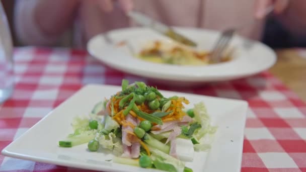 건강 한 야채와 햄 샐러드가 흰색 접시 위에 있습니다. 뒤에서 점심을 먹는 여자. — 비디오