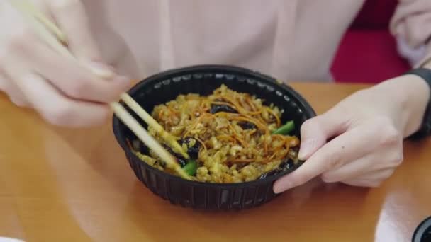 Donna mangia tagliatelle con carne, verdure e salsa con bastoncini di legno seduti in un ristorante fast food. — Video Stock