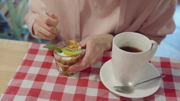 Woman in pink hoodie eating trifle dessert in a glass and drinking black tea. — Stock Video