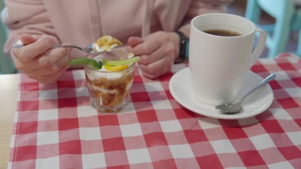 Hungry woman eating fruit trifle dessert in a glass and drinking black tea. — Stock Video