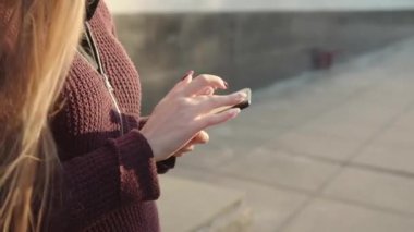Sokakta akıllı telefon kullanan, uzun saçlı bir kızın ellerini yakın plan çek..