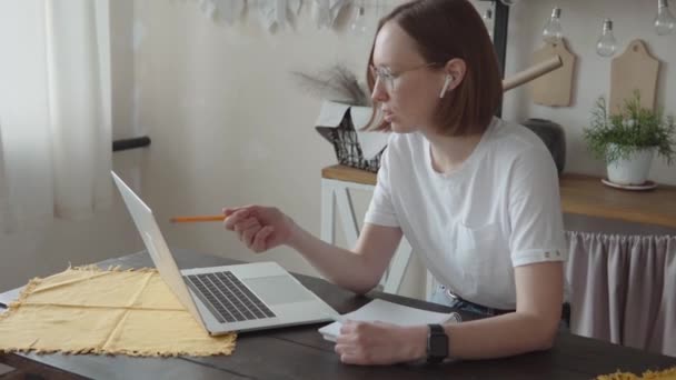 Gözlüklü ve kulaklıklı genç iş kadını bilgisayarını ve video konferans uygulamasını uzaktan kullanıyor.. — Stok video