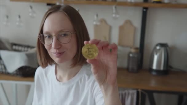 Студентка в очках держит в руке золотую монету биткойна. — стоковое видео