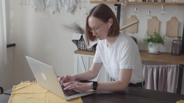 Kulaklıklı genç bir kadın işadamı evde oturup küresel salgın sırasında uzaktan çalışıyor. Kulaklıklı genç bir kadın işadamı dizüstü bilgisayarında mesaj yazıyor. — Stok video