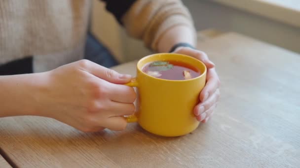 Крупный план женских рук на желтой кружке горячего цитрусового чая. — стоковое видео