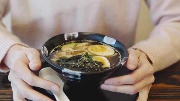 Közelkép egy ázsiai ételről egy japán étteremben. A női kezek egy tál csirkemell levest tartanak tojással és tésztával.. — Stock videók