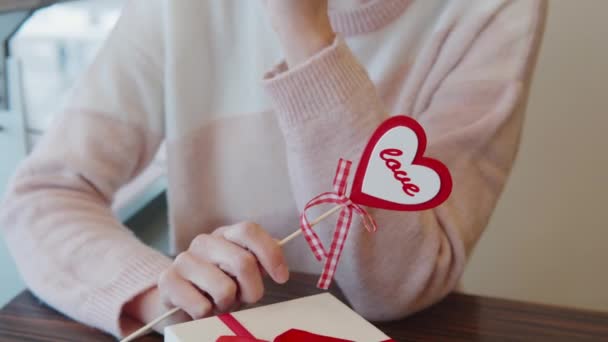 Menina agradável segurando o coração na mão perto de São Valentim Dia presente no restaurante. Conceito de data de aniversário de romance ou dia de São Valentim. — Vídeo de Stock