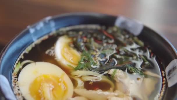 Közelkép egy ázsiai ételről egy japán étteremben. Miso leves csirkével, tojással, rizs tésztával, zöldhagymával, szezámmal és ébredéssel. — Stock videók