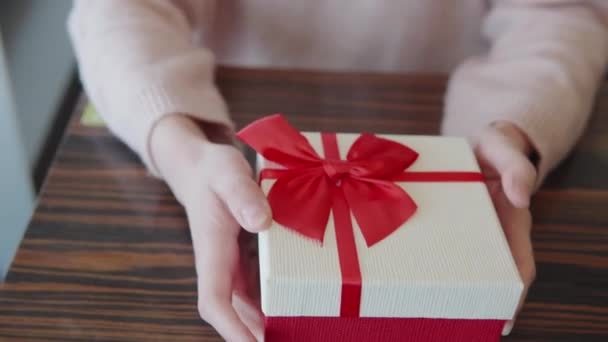 Κοντινό πλάνο των γυναικών χέρια με ένα κουτί δώρου κόκκινο και άσπρο χρώμα. Μια νεαρή γυναίκα πρόκειται να δώσει ένα δώρο στο σύντροφό της για διακοπές την ημέρα του Αγίου Βαλεντίνου, γενέθλια, Χριστούγεννα, επέτειο. Ρομαντικό — Αρχείο Βίντεο