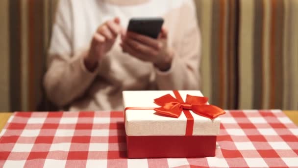 A menina planeja dar a seu amante um presente em cores brancas e vermelhas para o aniversário, Dia dos Namorados, aniversário. Uma mulher se senta em um restaurante e espera por um encontro conversando. Vista de perto. — Vídeo de Stock