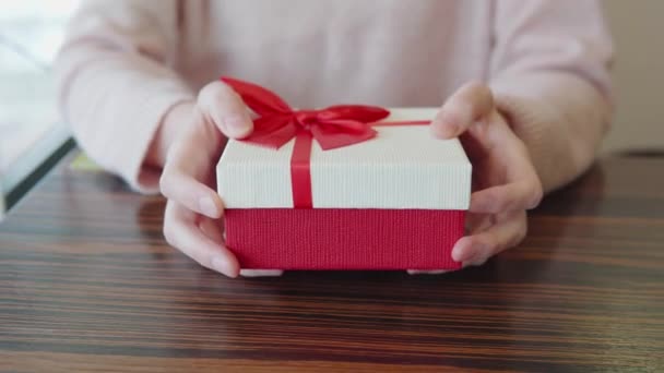 Presentación de un regalo para San Valentín, aniversario, cumpleaños, Navidad. Primer plano de una caja de regalo en manos de rojo y blanco con una cinta. Un momento romántico. — Vídeos de Stock