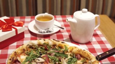 Önemli bir etkinlik için sofra kur: sıcak lezzetli pizza ve bir fincan bitkisel çay. Hediye kırmızı ve beyaz renkli güzel bir kutuda. Sevgililer Günü, yıldönümü, doğum günü konsepti.