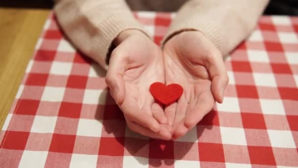Una chica bonita muestra un corazón rojo casero como símbolo de amor por un día de fiesta o aniversario de San Valentín. Un momento romántico durante una declaración de amor o una propuesta de matrimonio. — Vídeos de Stock